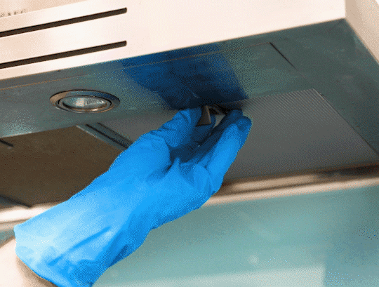 Woman in rubber gloves cleaning cooker hood in kitchen