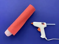 A red foam sheet is wrapped around the kitchen towel tube, leaving the yoghurt pot visible, and secured with the hot glue gun.