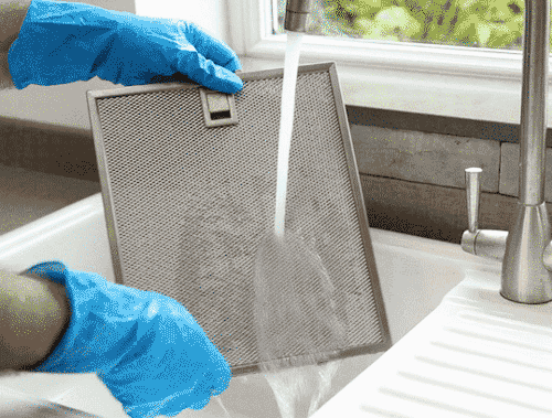 Hands in rubber gloves rinsing the cooker hood filter under running water