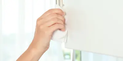 Hand wiping a kitchen cabinet door with a white cloth near the handle, cleaning the surface in a bright, modern kitchen.