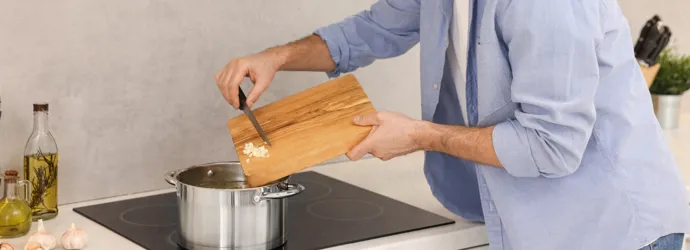 A man adds chopped garlic to a pot on an induction stove.
