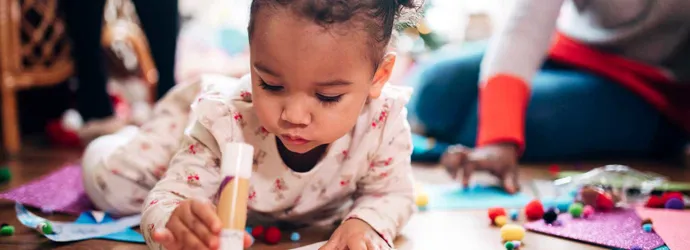 A little girl holding a glue stick while doing arts and crafts