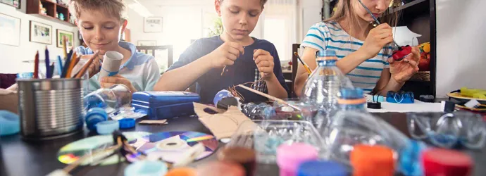 3 children learning how to reduce waste by making crafts from recyclable plastics and cardboard tubes