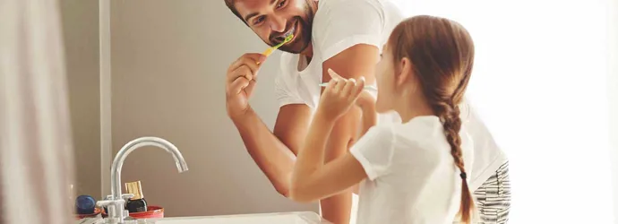 A man and his young daughter learning how to save water whilst brushing their teeth together in a bathroom
