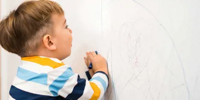 Ein kleiner Junge schreibt mit Stiften auf einer Tapete