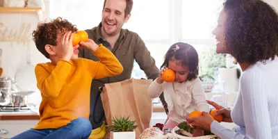 Two kids play with oranges; parents unpack groceries.