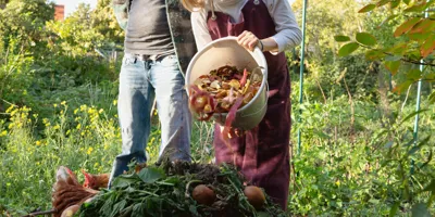 A person watches a girl empty out a bucket of vegetable scraps, demonstrating the difference between compostable and biodegradable
