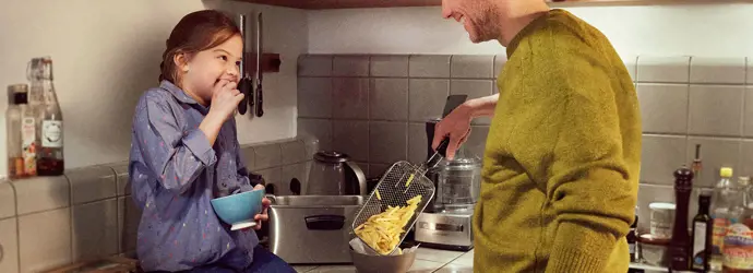 Dad and daughter in the kitchen preparing a meal for the family with french fries.
