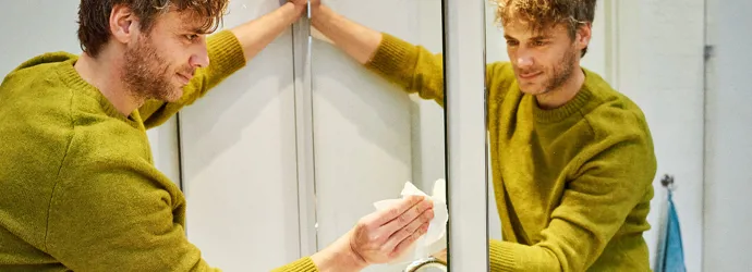 Man cleaning the mirror in the bathroom with a wipe leaving no streaks.
