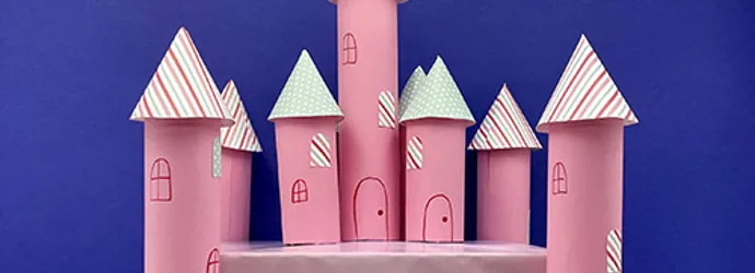 A pink cardboard castle with 7 kitchen towel tube towers around a rectangular base sits in front of a blue background.