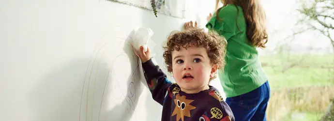 Zwei Kinder kritzeln mit Buntstiften auf eine harte Oberfläche und hinterlassen Stiftflecken.
