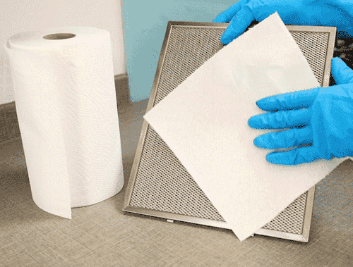Hands in rubber blue gloves drying the cooker hood filter with kitchen paper