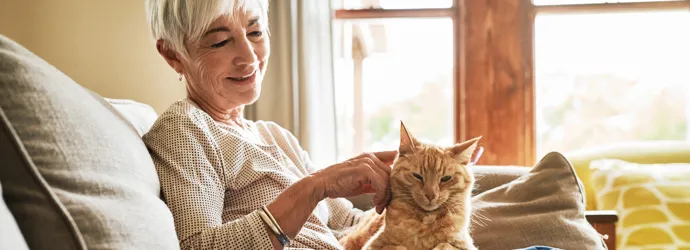 Smiling woman pets a ginger cat on her lap on the couch.