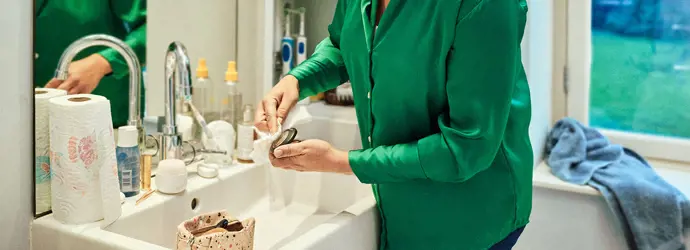 Woman in a green shirt, cleaning limescale off of the sink.
