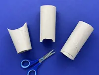 3 cardboard tubes are on a blue surface with the ends cut to the animal shapes with a pair of scissors below them.