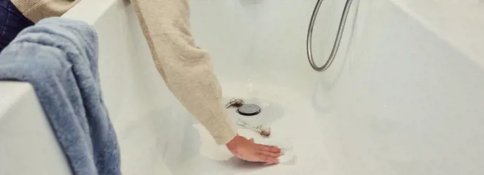 Woman removing hair from the drain in the bathtub.