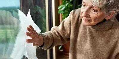 Old lady wearing a beige jumper cleaning a window.