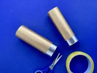 2 different width gold cardboard tubes with foil ends are laid next to a roll of tape and a pair of blue scissors.