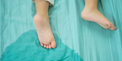 Two feet of a child lying on a wet bed in a green sheet.