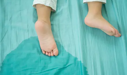 Two feet of a child lying on a wet bed in a green sheet.
