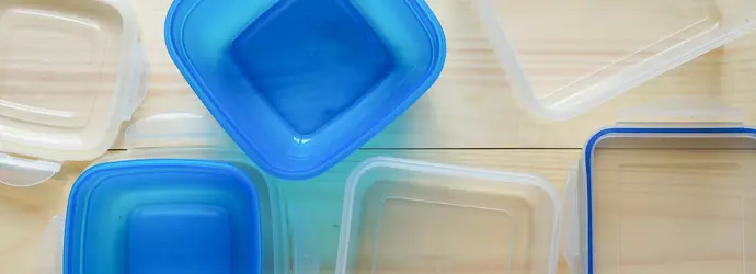 Assorted empty reusable Tupperware containers with blue and clear lids arranged on a light wooden surface.