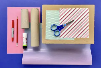Pens, cardboard tubes, a cardboard box, a glue stick, scissors and red-and-white striped paper laid on a blue background.