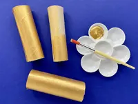 3 different width carboard tubes are painted gold and laid next to a paintbrush, white container, and gold paint.