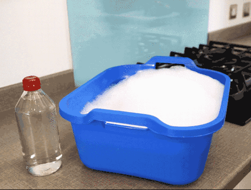 Hands in rubber gloves soaking the cooker hood in soapy water next to white vinegar