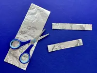 A long piece of foil is under a pair of blue-handled scissors with two smaller foil offcuts laid to the right.