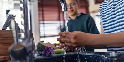 Boys rinse fresh veggies under tap in a modern kitchen.